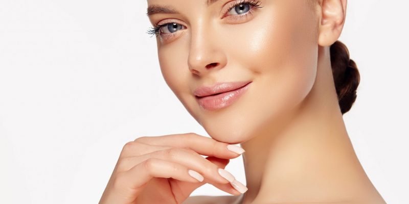 Beautiful young woman with clean fresh skin touching her face .